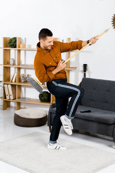 cheerful man dancing with broom in modern living room 