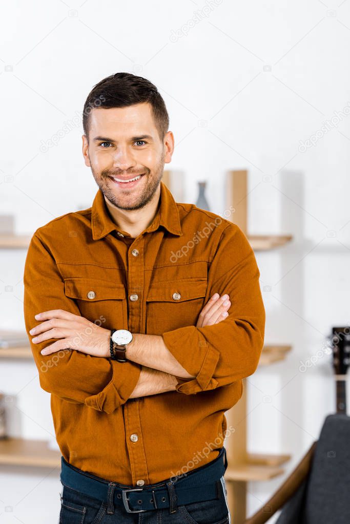 cheerful man standing with crossed arms in living room 