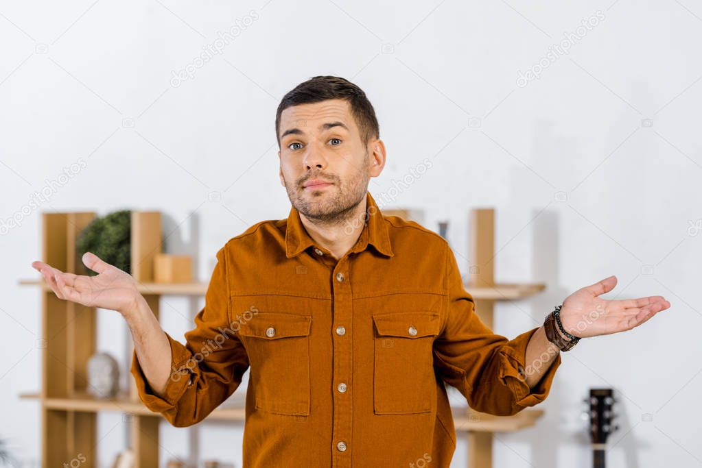 handsome man standing in modern living room and doing confuse gesture