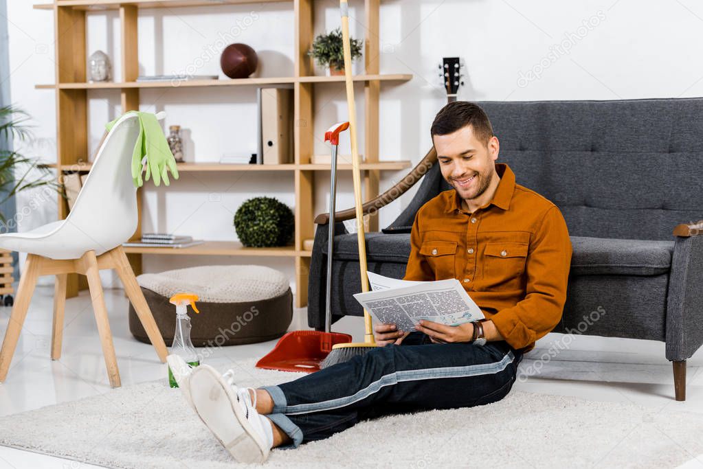 handsome man sitting on floor in modern living room and reading newspaper