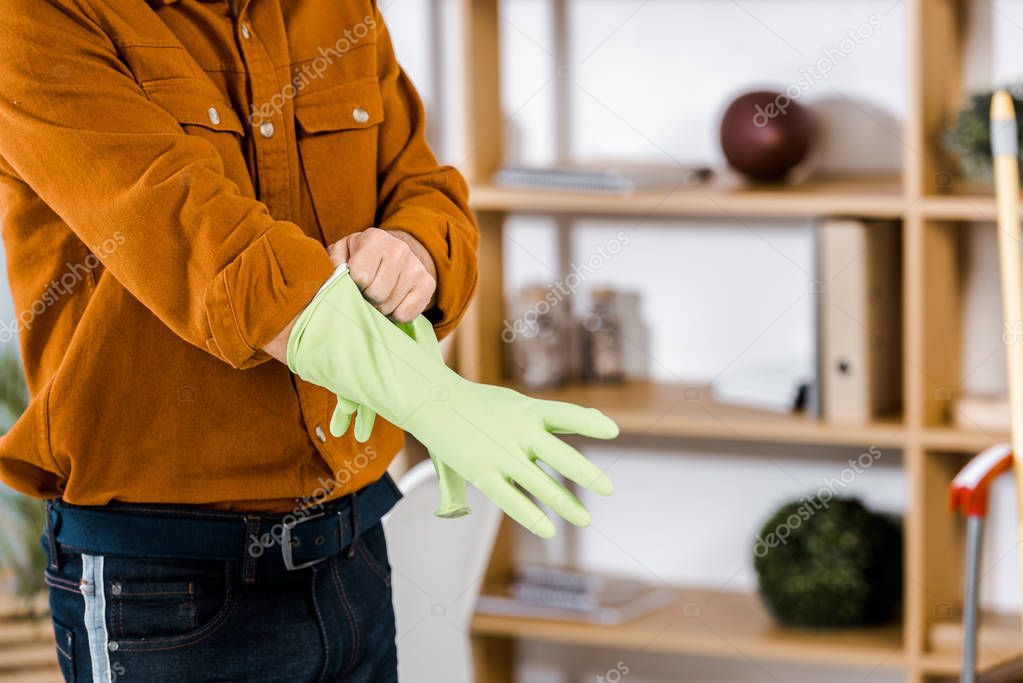 cropped view of man standing in modern living room putting up rubber gloves