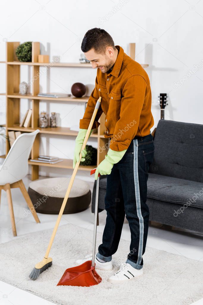 handsome man standing in modern living room and sweeping floor