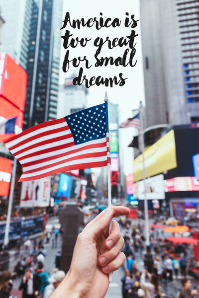 partial view of man holding american flag on new york city street with "america is too great for small dreams" quote