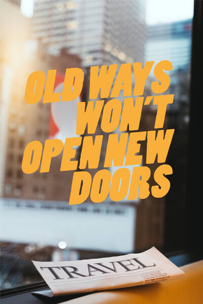 close up view of travel newspaper with "old ways wont open new doors" quote on window and new york city on background