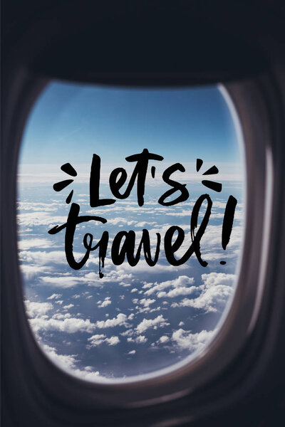 view of blue cloudy sky from airplane with "lets travel" lettering on window