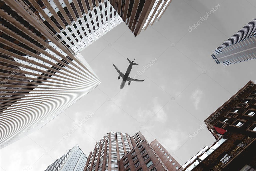 bottom view of skyscrapers and airplane in cloudy sky in new york city, usa