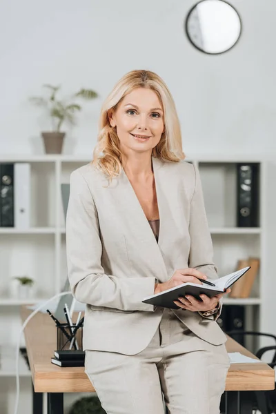 Happy Mature Businesswoman Writing Notepad Smiling Camera Office — Stock Photo, Image