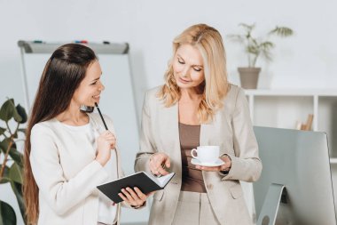 iş kadınları fincan kahve ve birlikte ayakta ve iş ofis tartışırken Not defteri ile gülümseyen