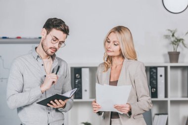 kağıtları tutarak ve defter ile gözlük genç işadamı bakarak olgun işkadını