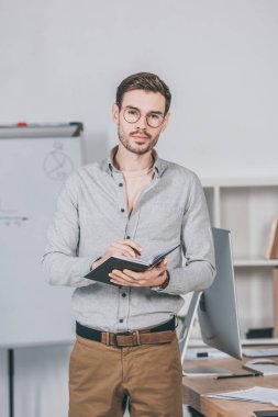 ciddi genç iş adamı Not defteri tutan ve kamera Office bakarak gözlük