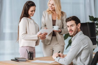 konuşurken iş kadınları ve genç işadamı kamera Office bakarak gülen