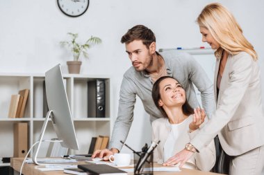 olgun iş akıl hocası genç meslektaşları Office masaüstü bilgisayarla çalışma bakarak gülen 