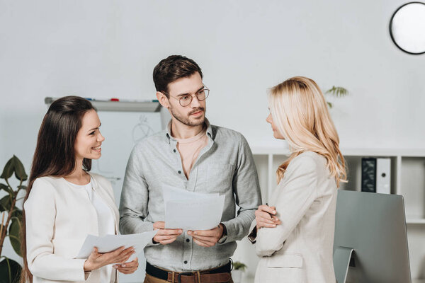 young coworkers holding papers and looking at mature businesswoman in office