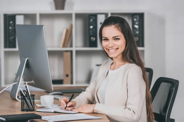 Happy Young Businesswoman Taking Notes Smiling Camera While Sitting Workplace — Stock Photo, Image