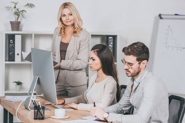 mature businesswoman holding folder and looking at young businesspeople working in office