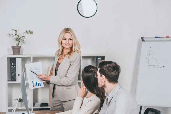 Lächelnder Business Mentor Zeigt Auf Diagramme Und Sieht Junge Kollegen — Stockfoto