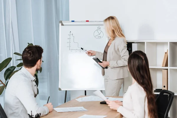 Business Mentor Pointing Whiteboard Charts While Young Colleagues Sitting Table — Stock Photo, Image