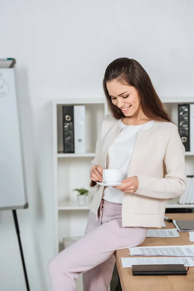 Sonriente Joven Mujer Negocios Sentada Escritorio Mirando Taza Café Oficina — Foto de Stock