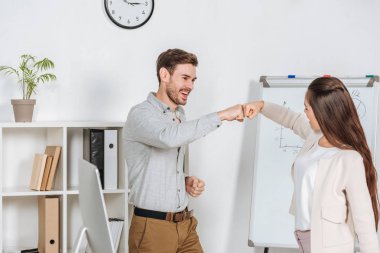 happy young businessman giving fist bump to smiling female coworker in office clipart