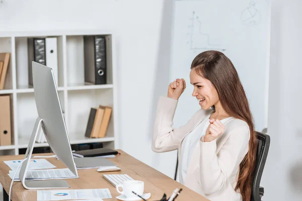 拳を振ると オフィスでデスクトップ コンピューターを見て幸せの若い実業家の側面図 — ストック写真
