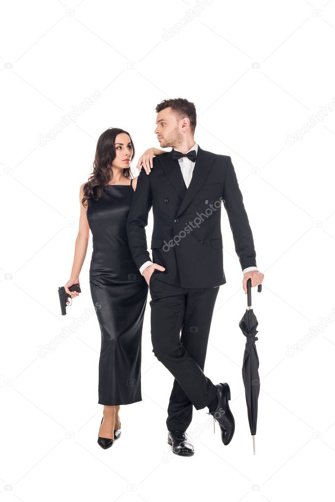 young elegant couple of killers in black clothes posing with gun and umbrella, isolated on white