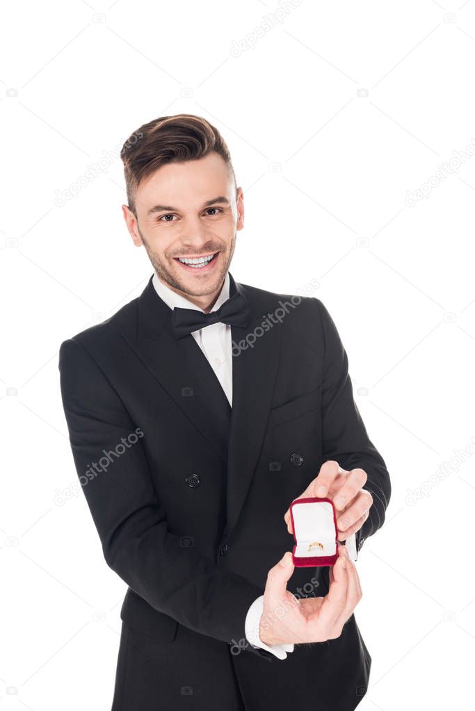 happy man in black tuxedo holding proposal ring in box, isolated on white