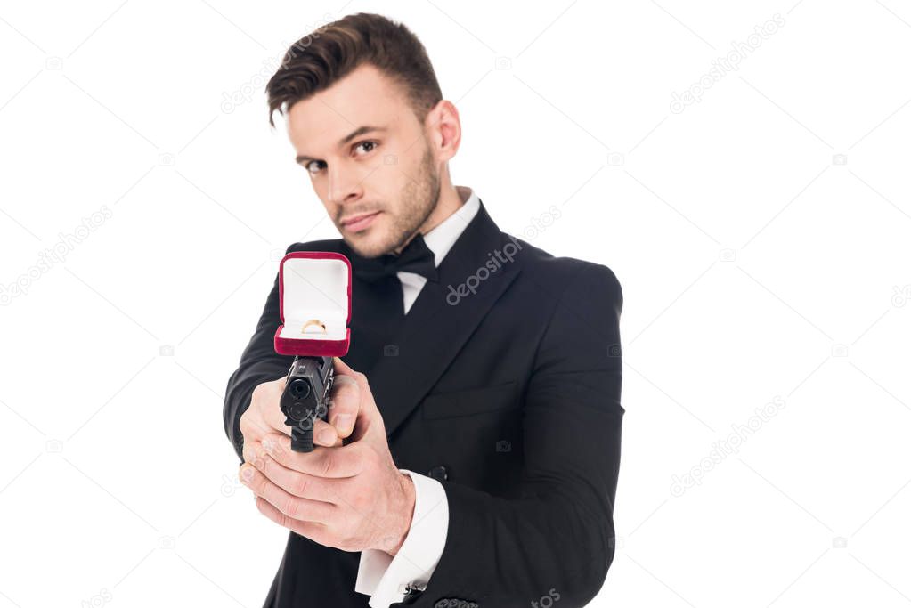 handsome secret agent in black suit aiming with handgun with proposal ring, isolated on white