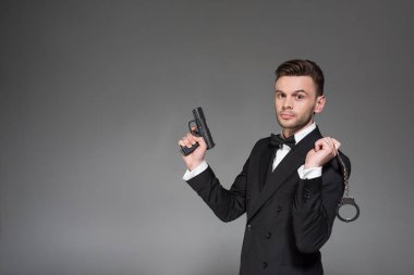 yakışıklı gizli ajan tabanca ve kelepçeleri, gri izole tutarak siyah elbiseli
