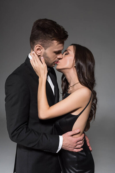 привлекательная элегантная пара целуется и обнимается изолированно на сером
 