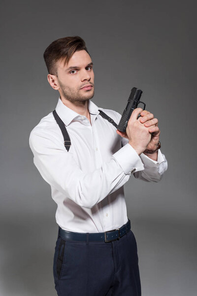 handsome male killer with holster holding handgun, isolated on grey