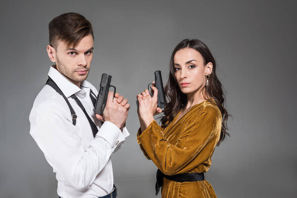 elegant confident couple of secret agents posing with handguns, isolated on grey