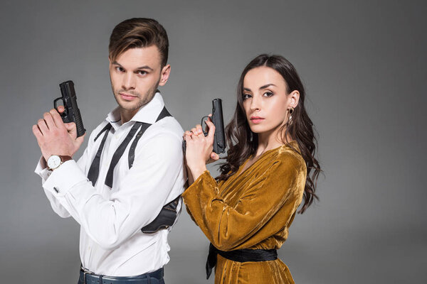 beautiful confident couple of secret agents posing with weapon, isolated on grey