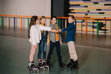 Smiling children in roller skates staying on roller rink and stretching hands together clipart