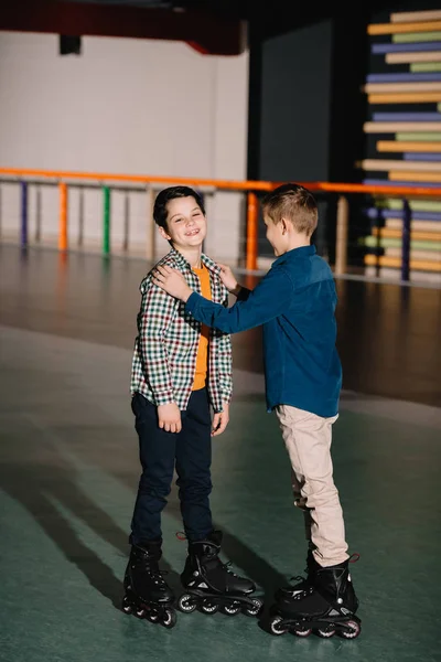 漂亮的男孩触摸笑的朋友 而站在宽敞的溜冰场 — 图库照片