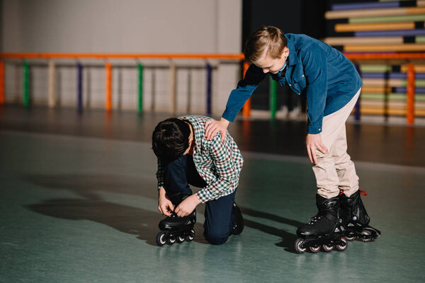 Pretty careful boy helping friend in fixing roller skate boot 