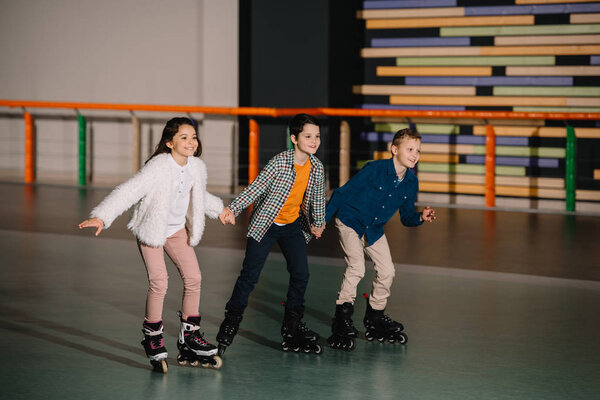 Three happy smiling children skating in roller rink with holding hands