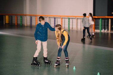 Joyful kids practicing roller skating on rink together clipart