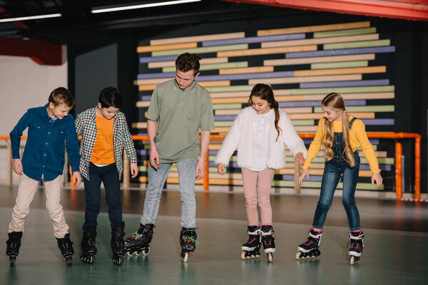Young trainer showing skating basic technics to attentive children 