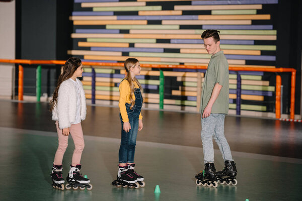 Двое милых детей внимательно слушают инструкции юных тренеров по катанию на коньках
