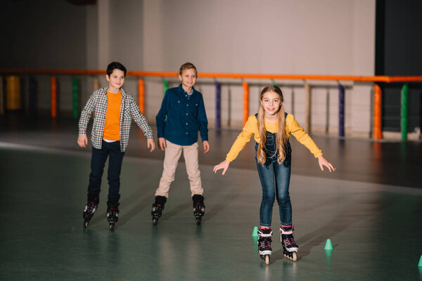 Улыбающиеся дети на роликовых коньках тренируются на катке
