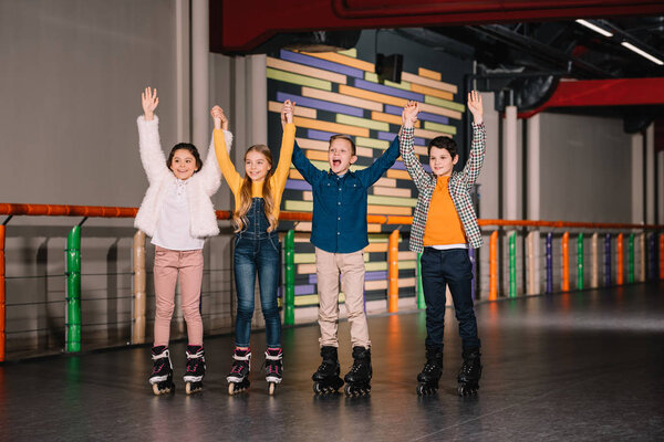 Cheerful kids in roller skates raising hands on skating rink