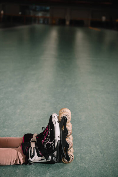 Partial view of child in skates sitting on roller rink