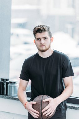 basketbol topu tutarak ve spor salonunda kamera bakarak yakışıklı genç sporcu