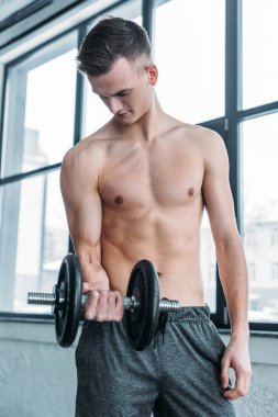 Dumbbell ile egzersiz ve spor salonunda pazı bakarak kas gömleksiz adam