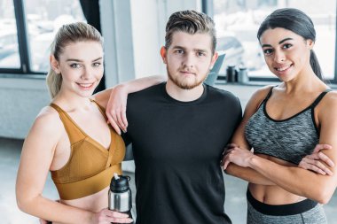 yakışıklı erkek eğitmen ile birlikte duran ve spor salonunda kamera gülümseyen güzel çok ırklı sportif kızlar