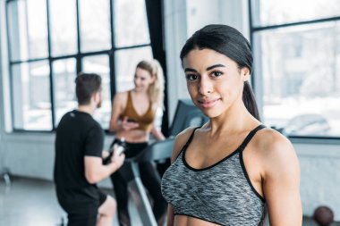 kameraya, genç arkadaşlar arkasında spor salonunda eğitim gülümseyen güzel Afro-Amerikan sporcumuz