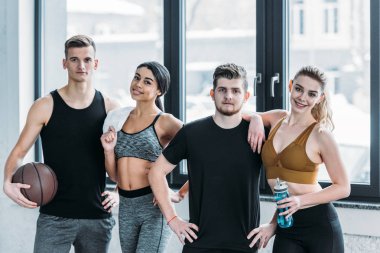 çok ırklı grup sportif genç arkadaşıyla birlikte ayakta ve spor salonunda kamera gülümseyen