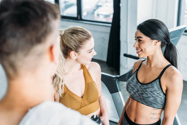 selective focus of young sportsman looking at cheerful sporty multiethnic girls smiling each other in gym