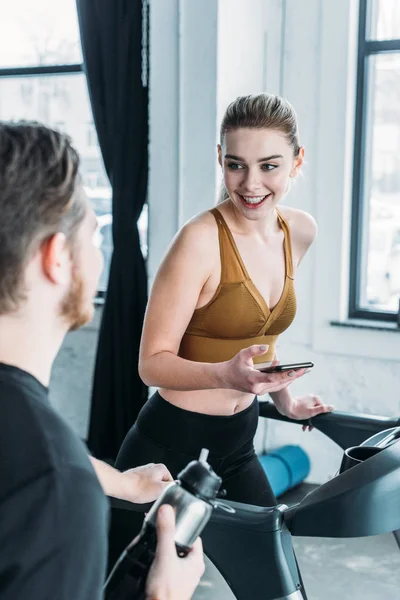 Smiling Sporty Girl Running Treadmill Looking Young Man Foreground Gym — Stock Photo, Image