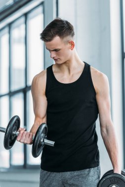 handsome young sportsman exercising with dumbbells in gym clipart